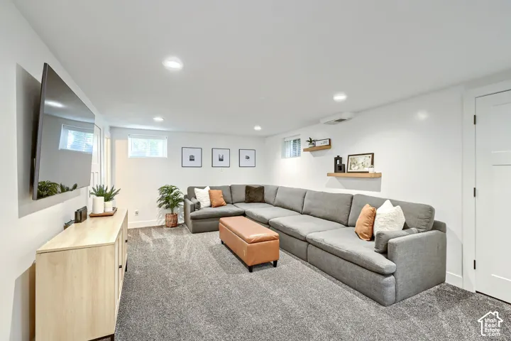 Neutral interior space featuring recessed ceiling lighting, wall-to-wall carpeting, dual floating wood-finish wall shelves, and multiple high-set windows