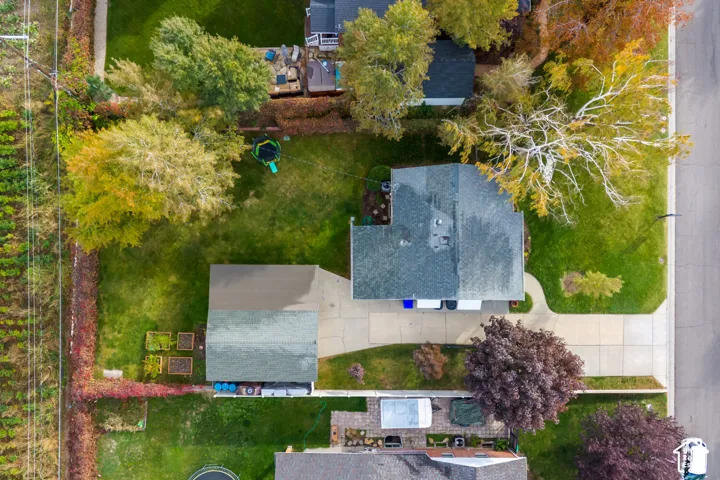 Aerial perspective of the property featuring a paved driveway, detached garage, mature trees, and expansive lawn space