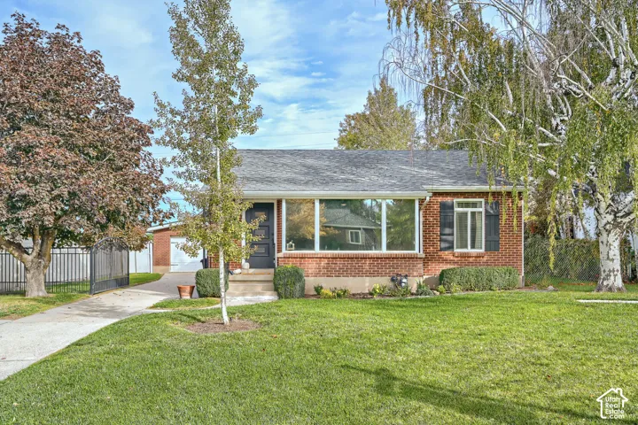 Red brick exterior featuring a multi-pane front window, asphalt shingle roof, paved driveway, and metal perimeter fencing