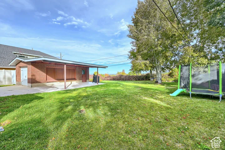 Spacious backyard featuring a manicured lawn, red brick structure with a covered patio, and mature trees