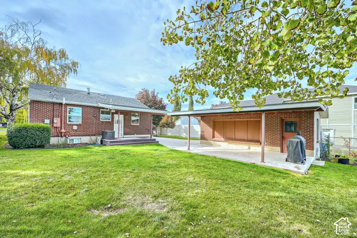 Brick exterior with a detached covered carport, concrete patio, and open lawn area