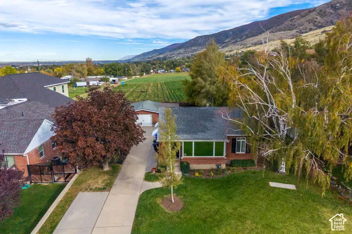 Brick exterior residence featuring a concrete driveway, detached garage, manicured lawn, and mountain backdrop