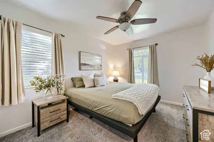 Neutral-toned bedroom featuring carpeting, multi-pane windows with hardware, and a ceiling fan with integrated lighting