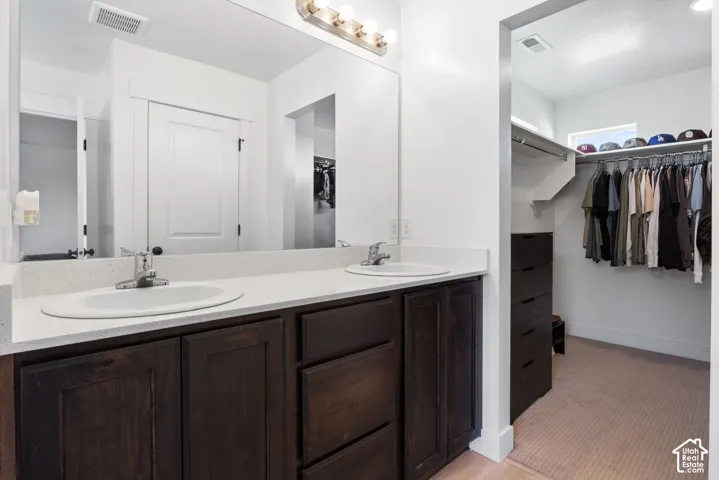 Double vanity featuring dark-stained cabinetry, light-toned composite countertops, oval undermount sinks, and a full-width mirror