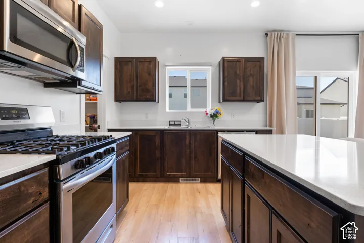 Kitchen featuring dark wood-finish cabinetry, quartz countertops, a central island, stainless steel appliances, and wood-finish flooring