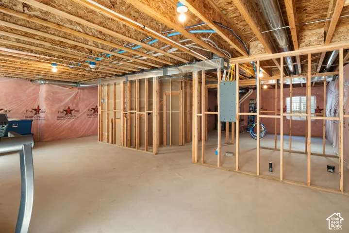 Unfinished basement featuring exposed wood joists, framed wall partitions, pink fiberglass insulation, and a concrete floor