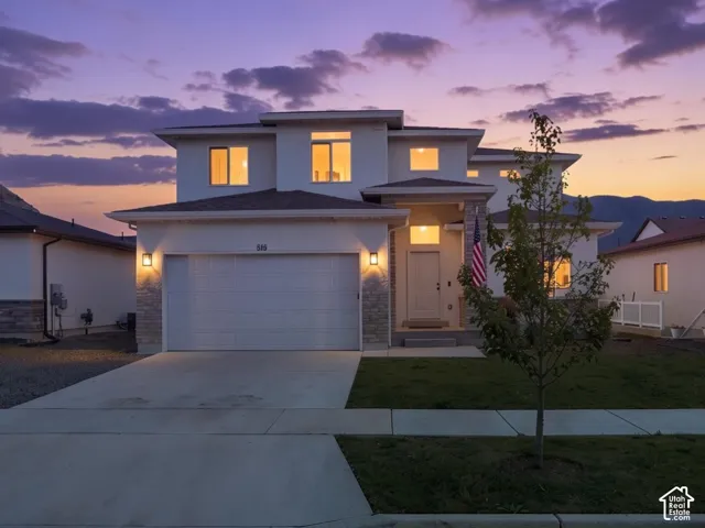 Two-story residence featuring light-toned exterior cladding, stone veneer accents, a multi-car garage, and concrete driveway