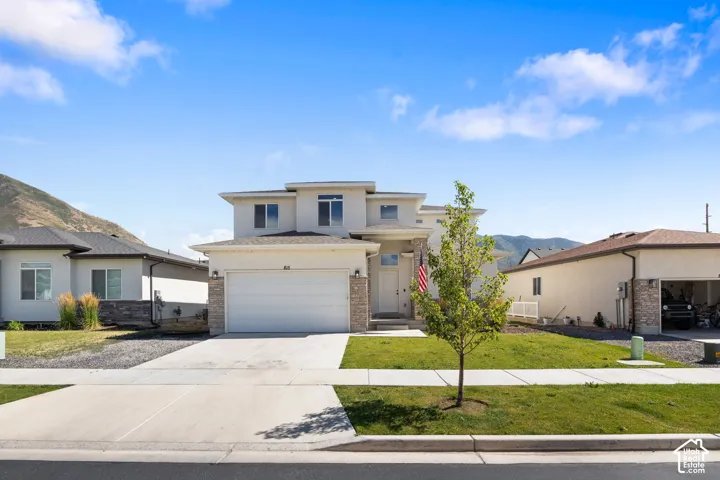 Two-story exterior featuring a light-colored stucco facade, stone veneer accents, an attached two-car garage, and a concrete driveway