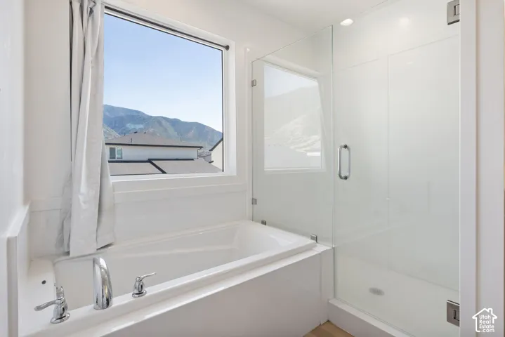 Built-in soaking tub with chrome fixtures, glass-enclosed shower, and mountain backdrop