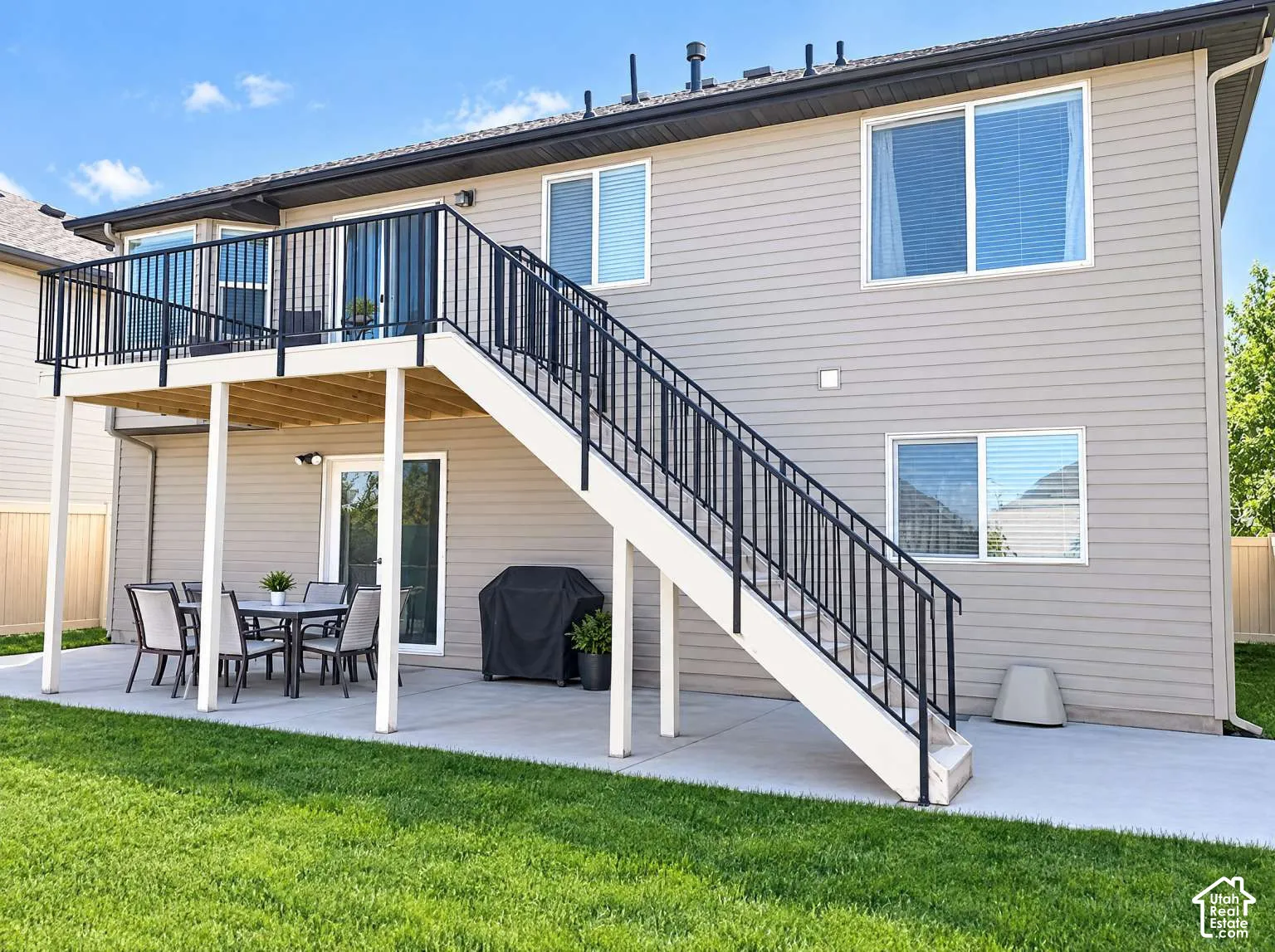 Rear exterior featuring horizontal lap siding, an elevated wood-framed deck with black metal railing, a concrete patio, and a set of exterior stairs with matching metal railing