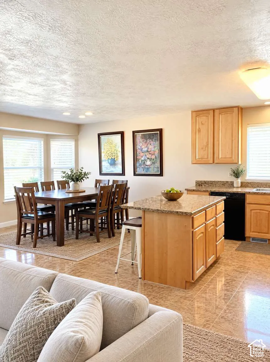 Kitchen featuring wood cabinetry, stone-surface countertops, central island, and tile flooring, paired with a multi-windowed alcove