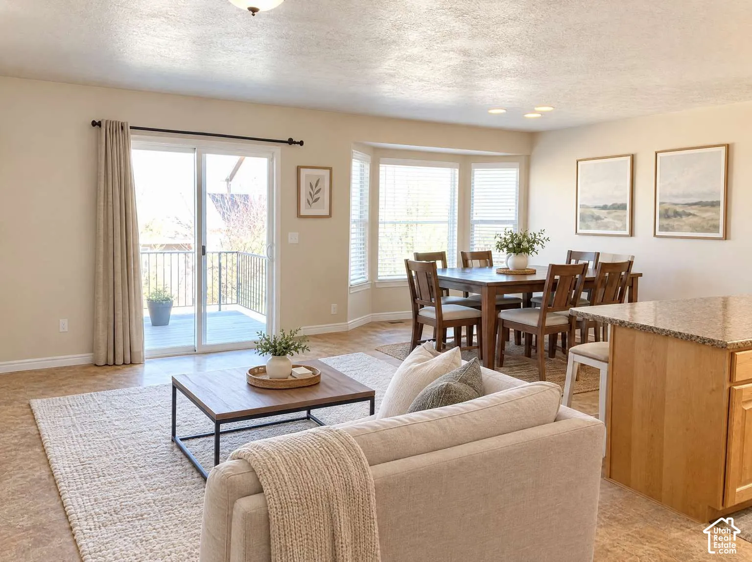 Open-concept interior featuring light-toned flooring, large bay windows, and a glass sliding door leading to an outdoor deck