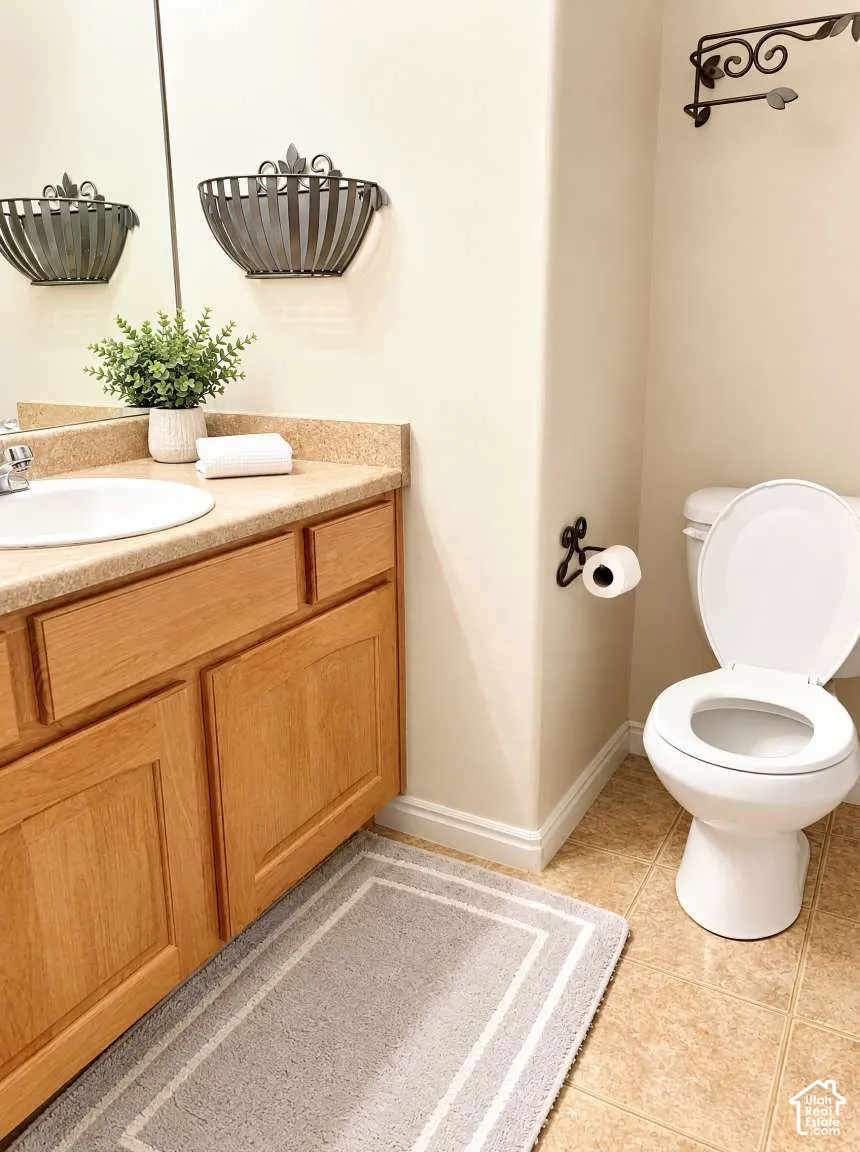 Bathroom featuring a wood-finish vanity with a composite countertop and integrated basin, ceramic tile flooring, and decorative wrought-iron wall-mounted hardware