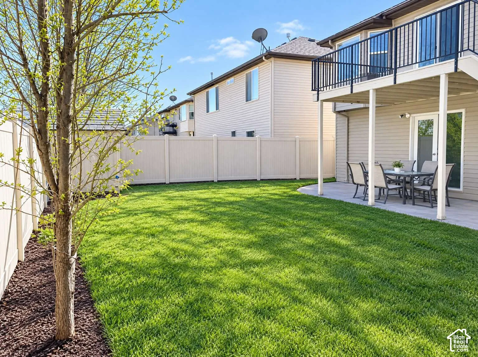 Backyard featuring a manicured lawn, full-height vinyl perimeter fencing, stone-paver patio, and an elevated deck with black metal railing
