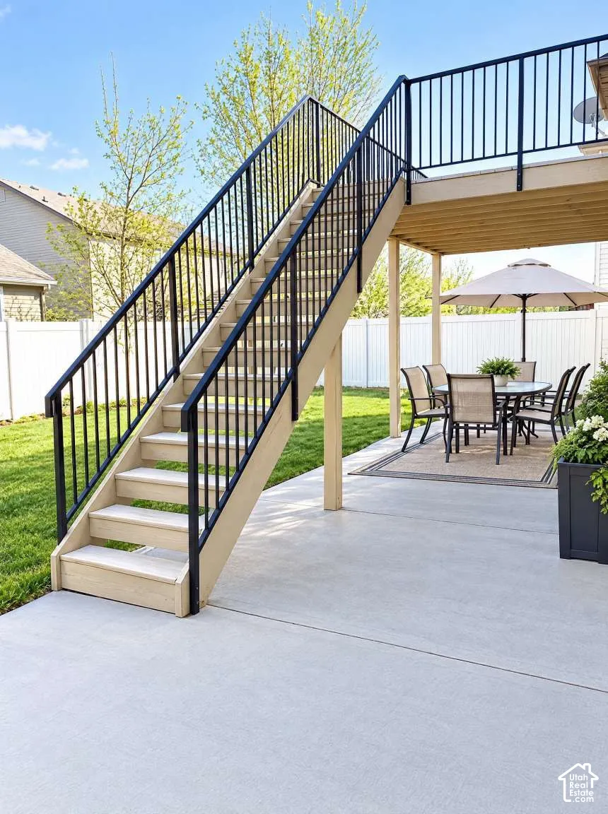 Concrete patio featuring a covered area, wood-finish staircase with black metal railings, and a fenced backyard