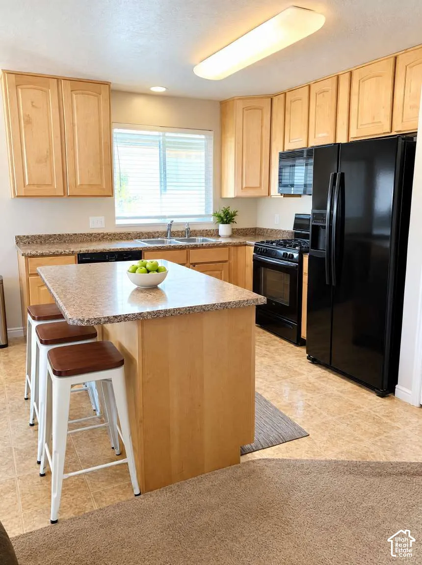 Kitchen featuring light wood cabinetry, stone-finish countertops, a center island, and black appliances