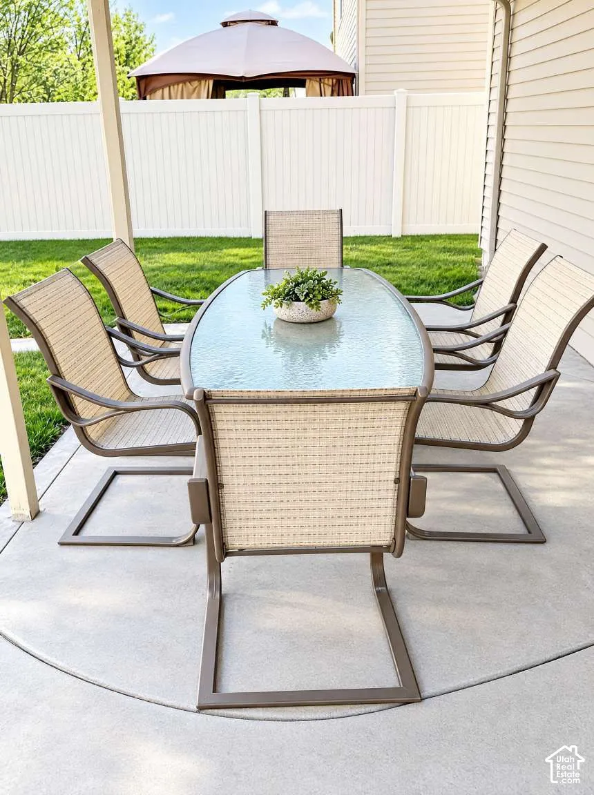 Covered concrete patio featuring a white vinyl privacy fence and manicured lawn
