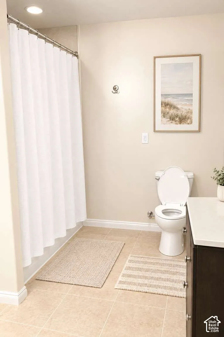 Bathroom featuring neutral tile flooring, a tub-shower combination with a metal curtain rod, a white toilet, and a vanity topped with a solid-surface countertop
