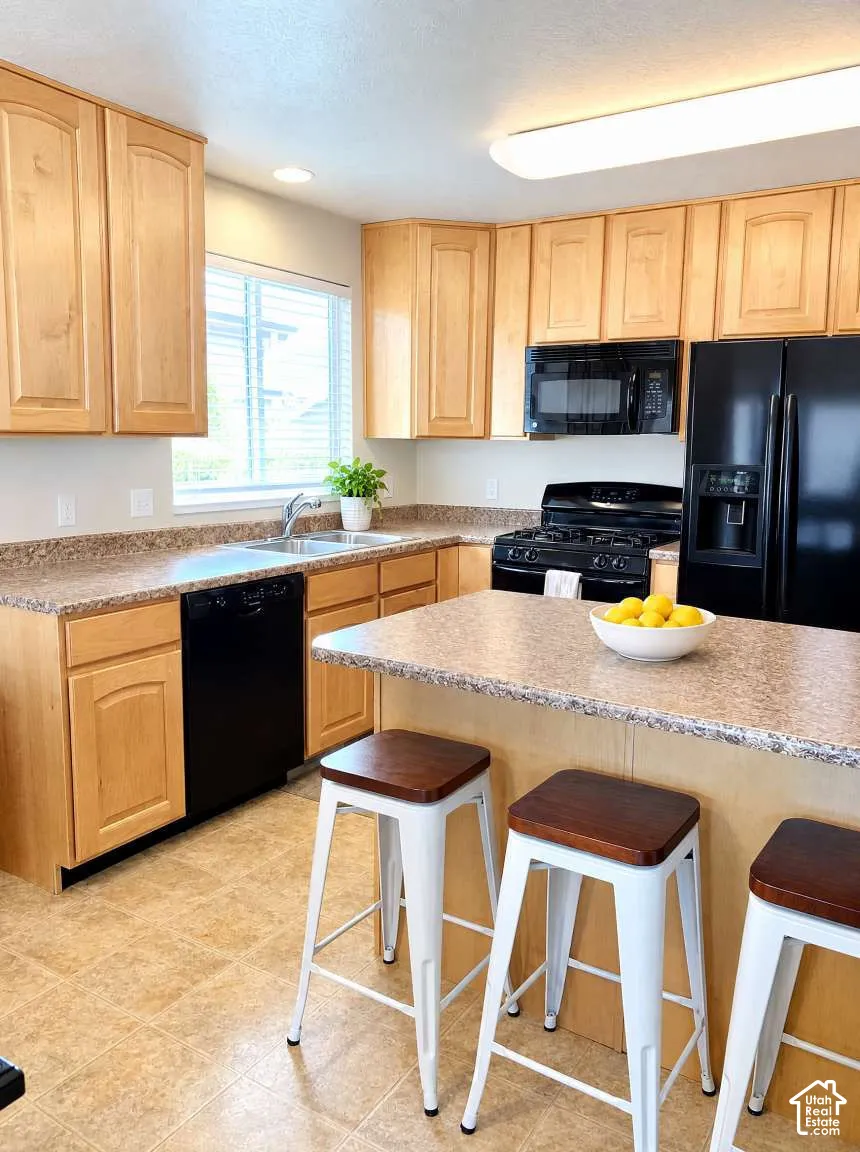 Kitchen featuring light-finish cabinetry, stone-texture countertops, integrated black appliances, a central island, and tile flooring