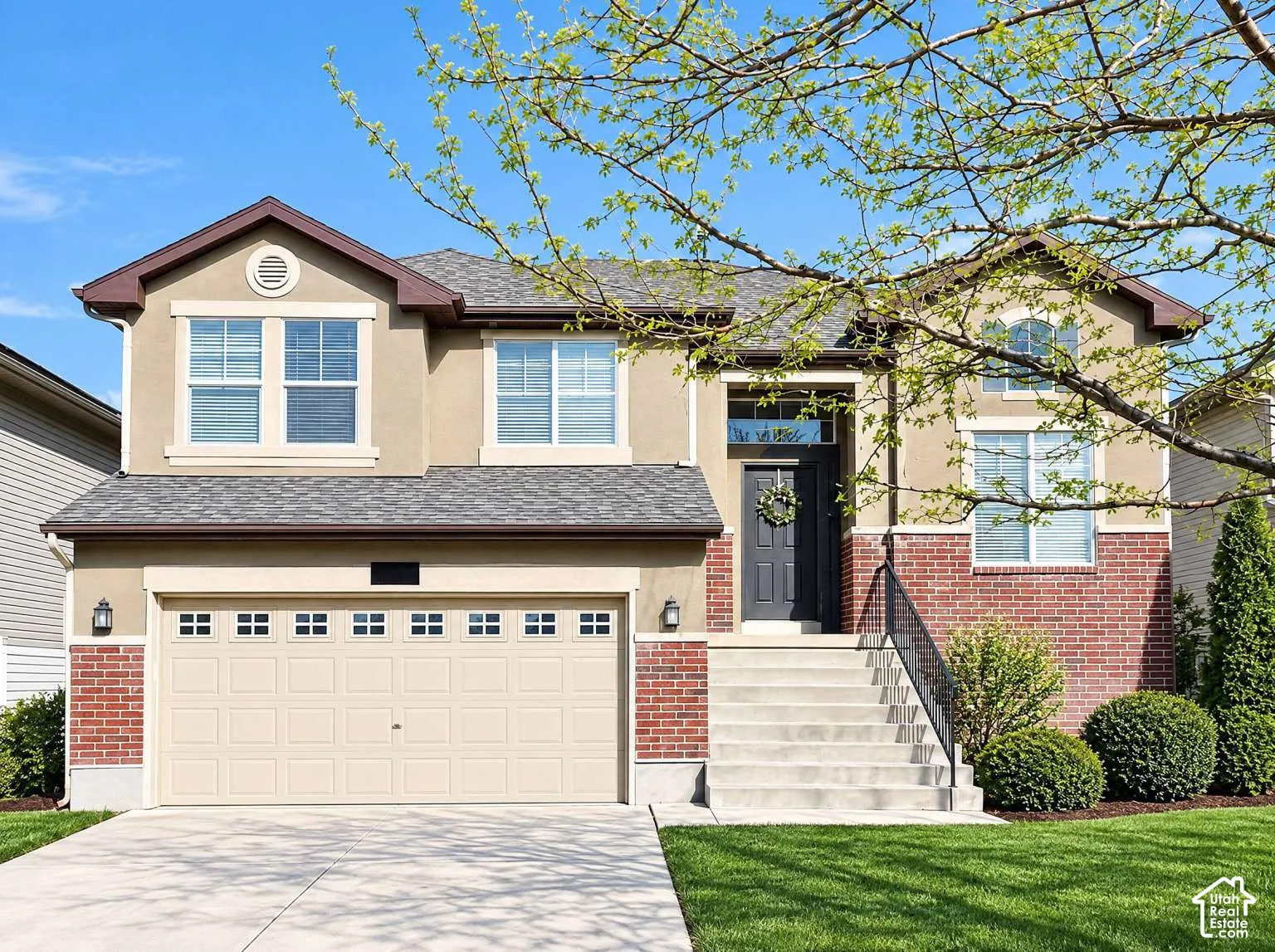 Two-story exterior featuring a mix of stucco and brick siding, a multi-paneled garage door, asphalt shingle roofing, and an elevated concrete entry staircase with metal handrail