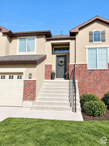 Exterior facade featuring a stucco finish with red brick accents, an arched-top window with shutters, a multi-pane entry door with a transom window, and a concrete staircase with a metal handrail