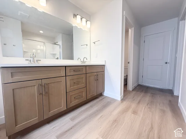 Dual-sink vanity with wood-finish cabinetry, solid surface countertop, wide wall-mounted mirror, and wood-finish flooring