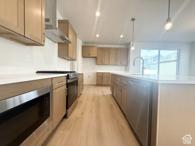 Kitchen featuring light wood-finish cabinetry, quartz countertops, stainless steel appliances, wood-finish flooring, and pendant lighting
