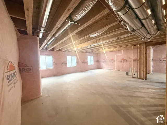 Unfinished lower level featuring exposed wood framing, concrete flooring, pink batt insulation, and dual metallic HVAC ductwork