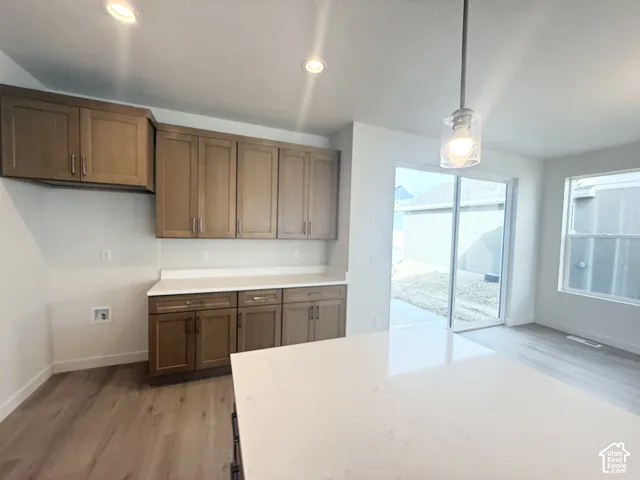 Wood-finish cabinetry with flat-panel doors, solid surface countertops, recessed lighting, pendant lighting, and sliding glass doors