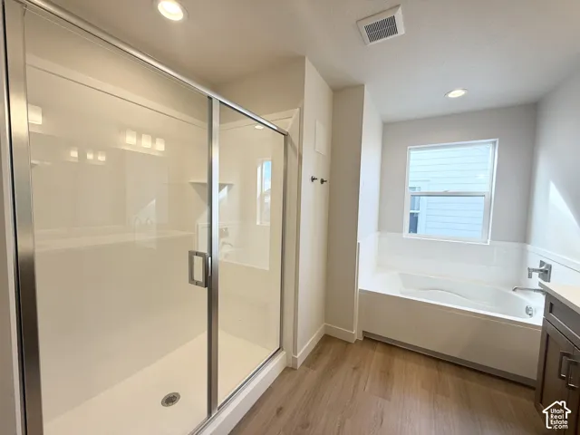 Glass-enclosed shower with a white surround, deep soaking tub with a tiled deck, wood-finish flooring, and recessed ceiling lighting