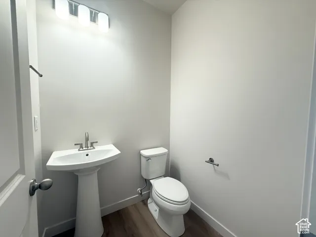 Pedestal sink with a polished chrome faucet, white ceramic toilet, wood-finish flooring, and a three-light fixture