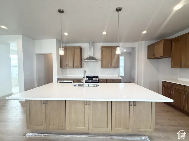 Kitchen featuring a large central island with a solid-surface countertop, shaker-style wood cabinetry, a stainless steel chimney-style range hood, and dual pendant lighting fixtures