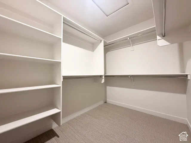 Walk-in closet featuring white built-in shelving, multi-level metal garment rods, and neutral carpeting