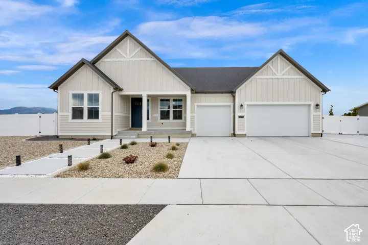 Single-story residence featuring vertical board-and-batten siding, a covered entryway, a three-car garage, and hardscaped landscaping with a concrete walkway