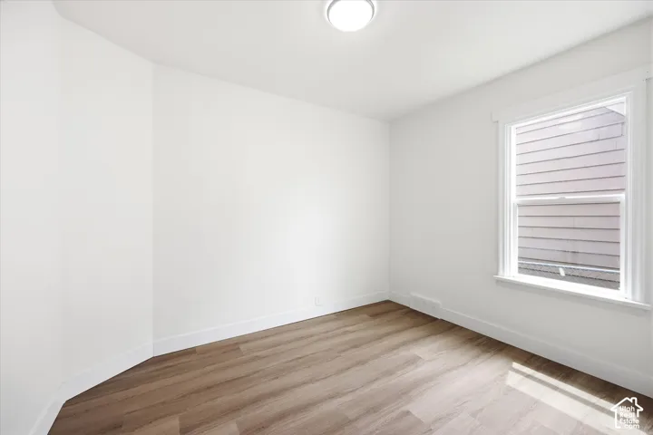 Neutral room featuring wood-finish flooring, white walls, a single-hung window with white casing, and a ceiling-mounted light fixture
