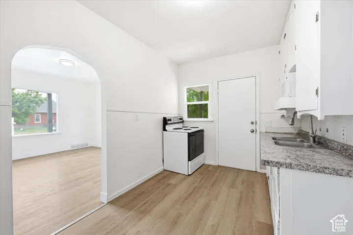 Kitchen featuring wood-finish flooring, stone-patterned countertops, white cabinetry, and an arched entryway