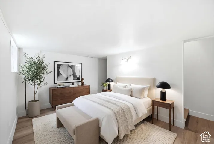 Bedroom featuring wood-finish flooring, white walls, and wall-mounted lighting