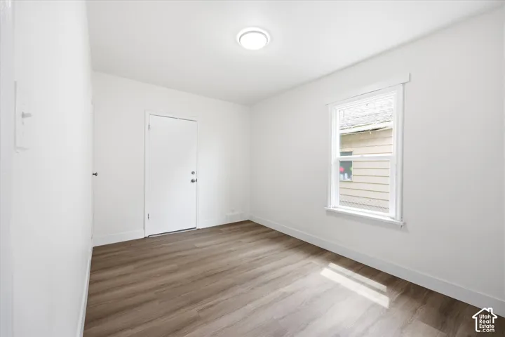 Interior space featuring wood-finish flooring, white walls, a single-hung window with casing, a solid-core door, and a flush-mount ceiling light