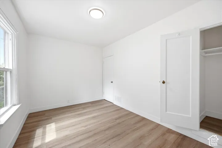 Neutral-toned interior featuring wood-finish flooring, a single-hung window, flush-mount ceiling lighting, and a closet with a built-in rod and shelf