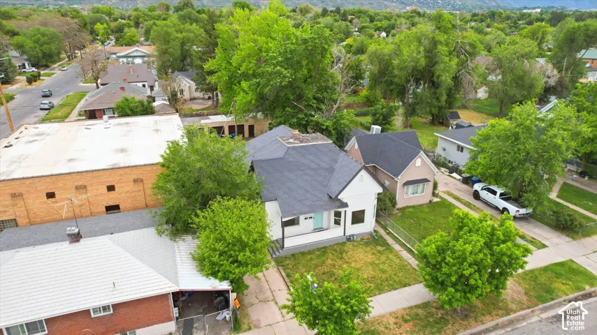 Single-story residence featuring a dark shingled roof, white exterior siding, a covered front porch, and mature trees