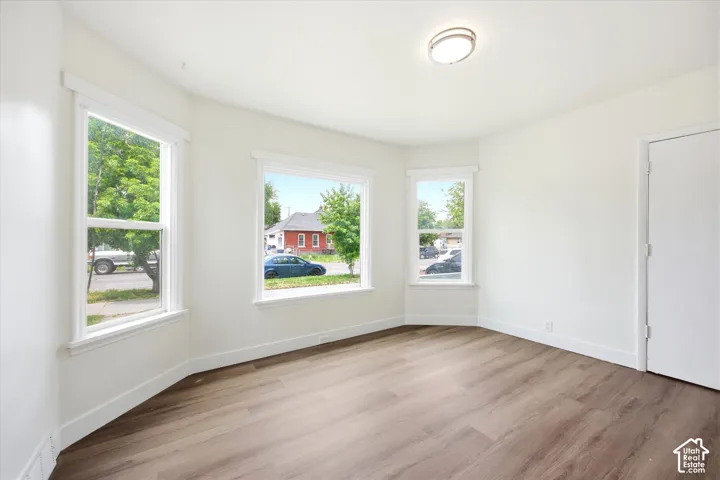 Room featuring wood-finish flooring, white walls, large bay-style windows, and a flush-mount ceiling light fixture