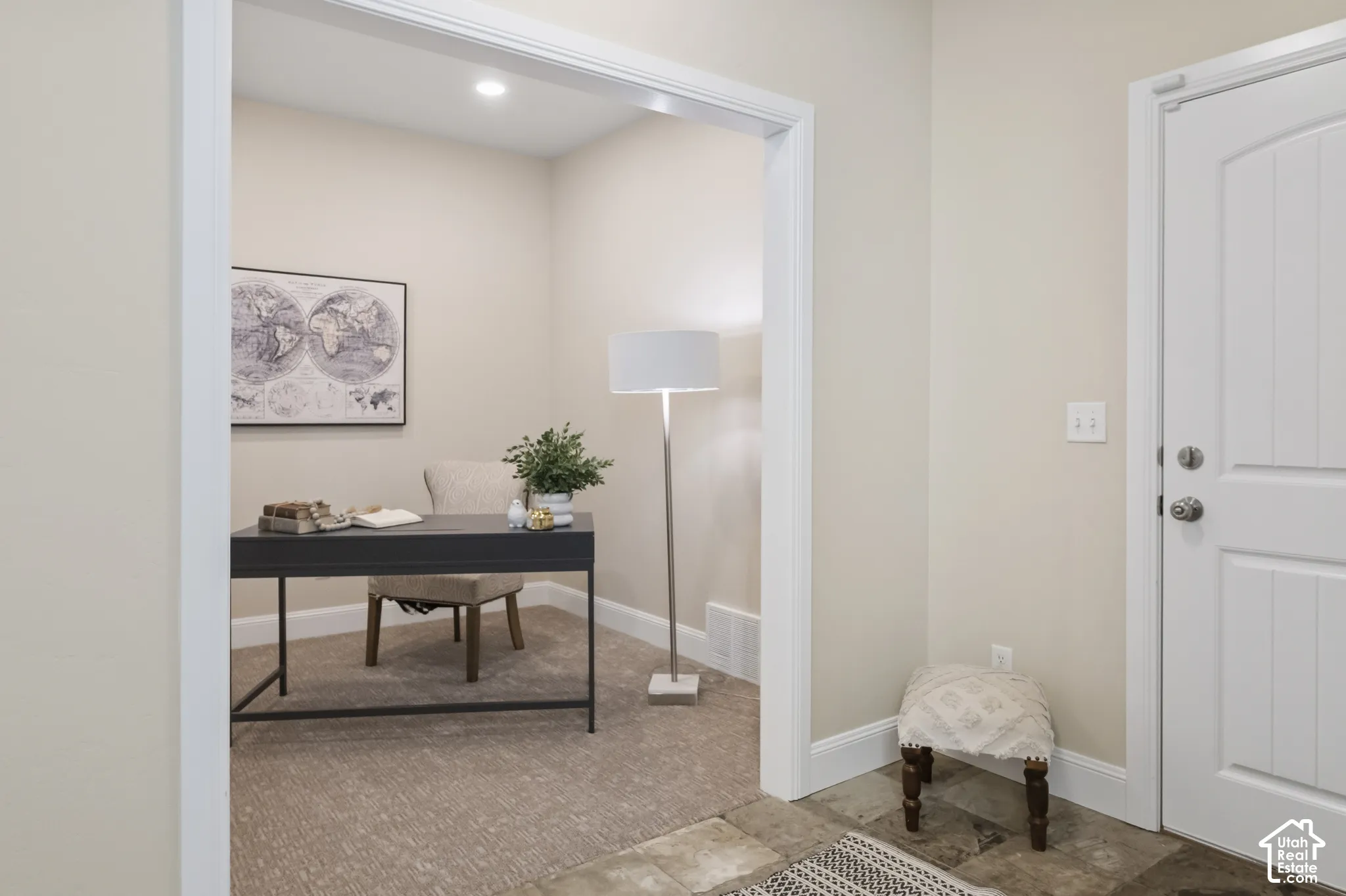 Ground floor entry with stone slate flooring and adjacent home office/den with neutral interior featuring wide-frame cased openings, textured carpeting, recessed lighting, and a paneled entry door with satin nickel hardware