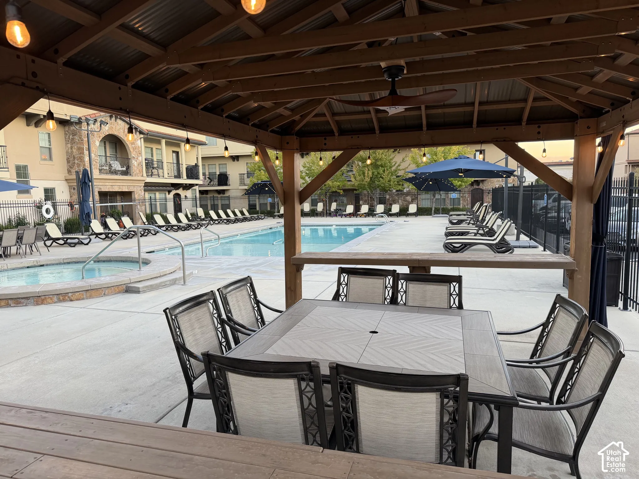 Covered timber-frame pavilion featuring a metal roof, ceiling fan, and string lighting, complemented by a swimming pool, integrated spa, and concrete deck