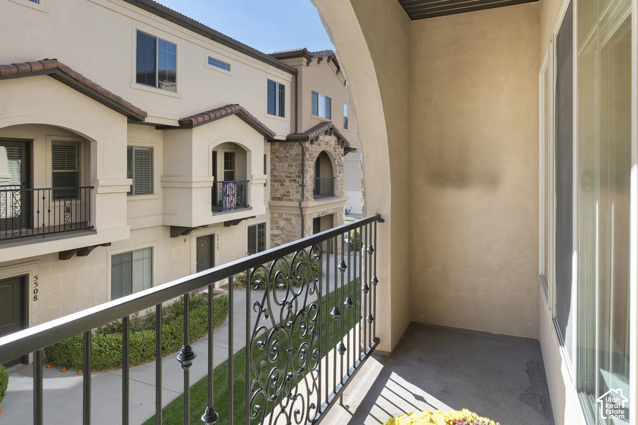 Covered balcony featuring ornamental metal railing, stucco exterior finishes, and arched architectural elements