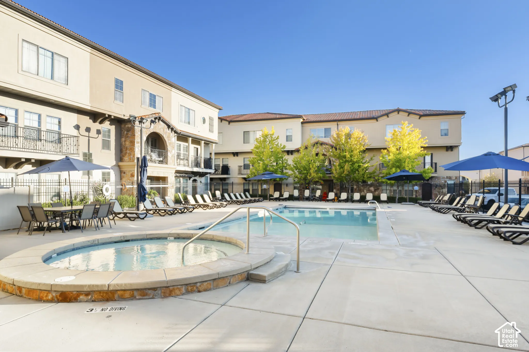 Outdoor swimming pool and stone-accented hot tub with concrete pool deck and metal perimeter fencing
