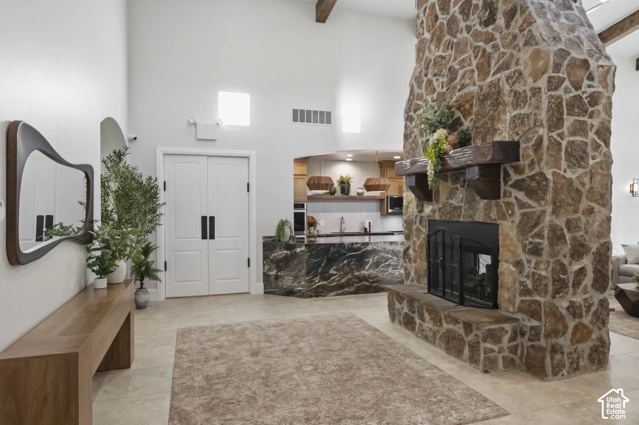 Clubhouse floor-to-ceiling stone fireplace with a thick timber mantel, vaulted ceiling with exposed wood beams, and natural stone flooring
