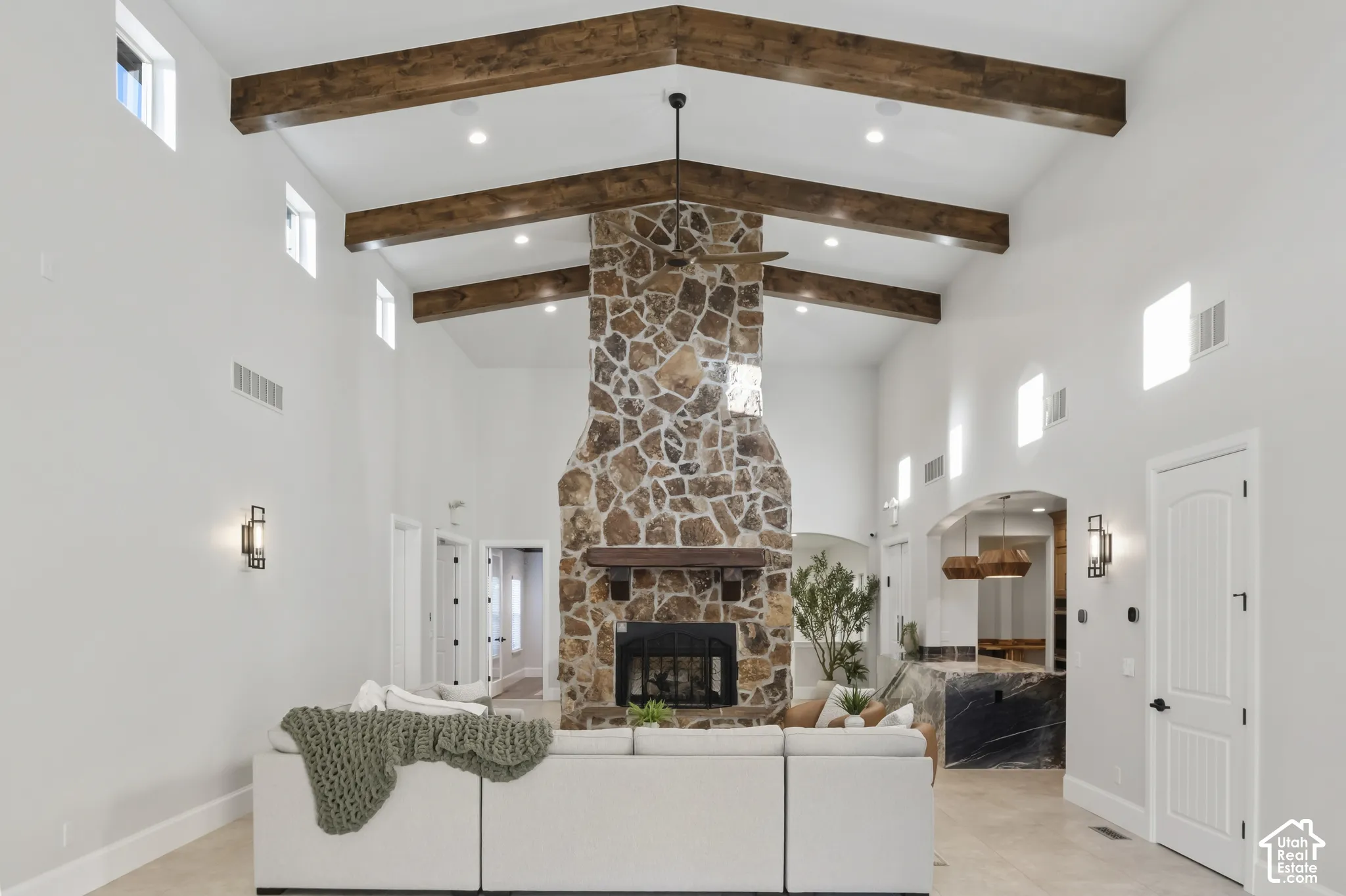Vaulted ceiling with exposed wood beams, floor-to-ceiling stone fireplace, heavy wood mantel, recessed lighting, and clerestory windows