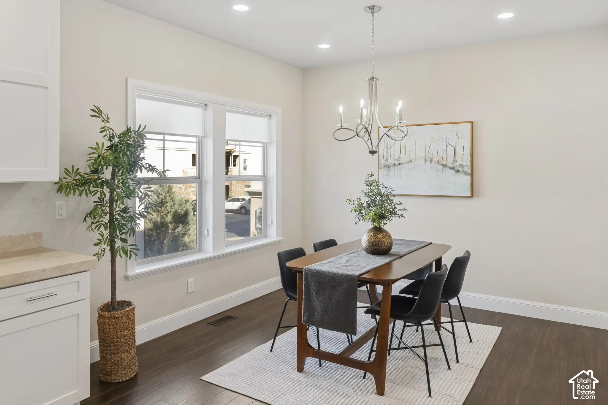 Large kitchen dining area with wood-finish flooring, recessed lighting, multi-arm chandelier, and white cabinetry with a marble stone-surface countertop