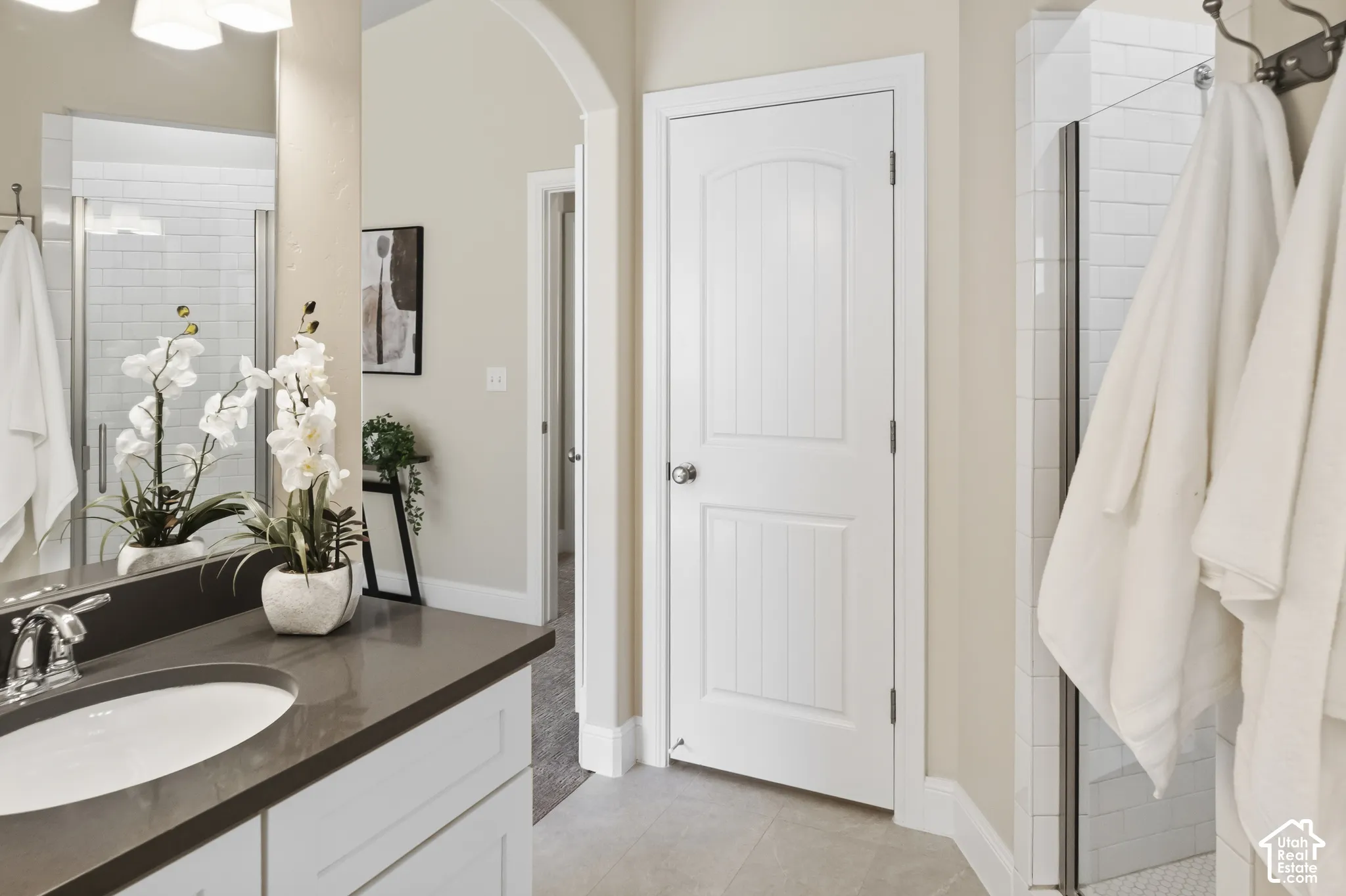 Primary bathroom featuring a white vanity with a solid-surface countertop, an oval under-mount sink, chrome faucet hardware, and a glass-enclosed shower with subway tile surround