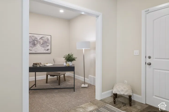 Ground floor entry with stone slate flooring and adjacent home office/den with neutral interior featuring wide-frame cased openings, textured carpeting, recessed lighting, and a paneled entry door with satin nickel hardware